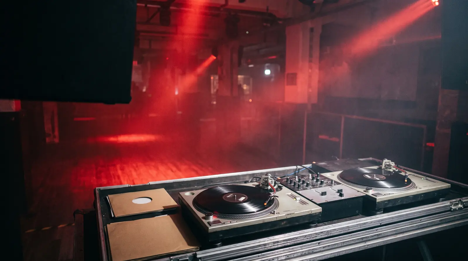 KI-Konzeptbild: zwei silberne Vinyl-Plattenspieler mit Battle-Mixer an einem DJ-Pult, Club in rotem Licht, keine Personen